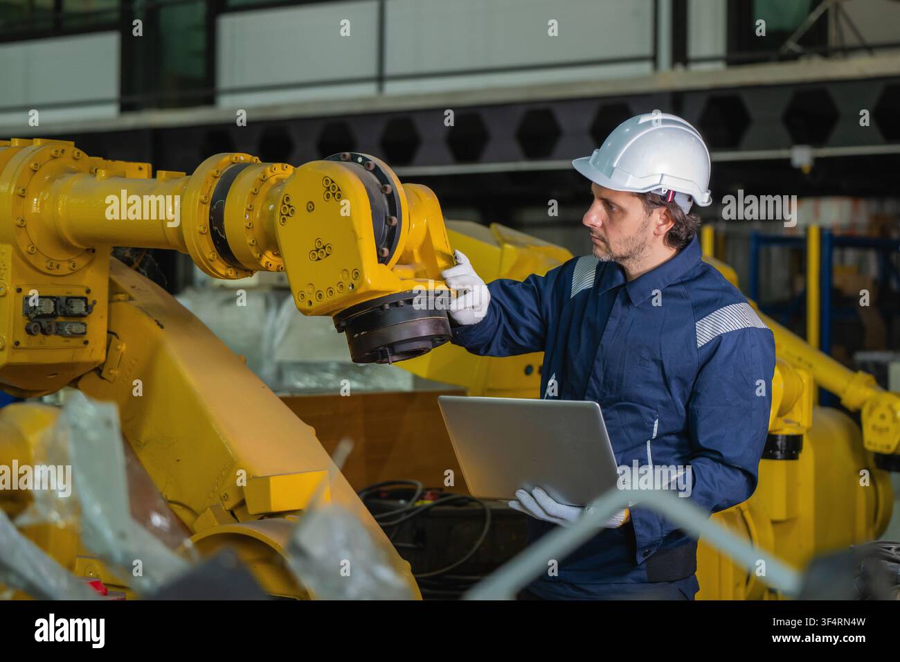 Ingénieurs industriels inspectant des stocks de bras robotiques jaunes dans un entrepôt d'usine. Concept de service de maintenance de machines industrielles lourdes, équipement qu Banque D'Images
