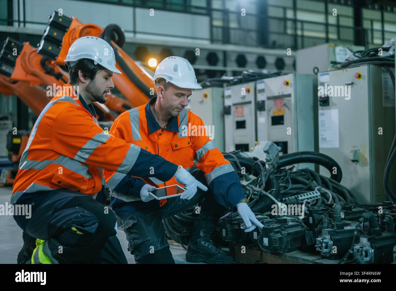 Équipe de techniciens en automatisation tenant une tablette numérique vérifiant l'équipement moteur robotique dans un atelier de contrôle qualité. Concept de réparation de machines lourdes, technologie Banque D'Images