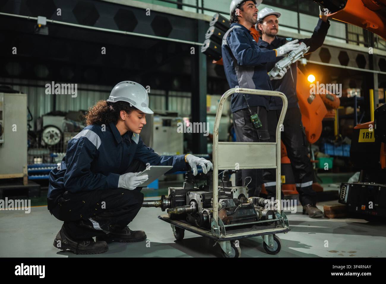 Ingénieure industrielle vérifiant des pièces de machines à bras robotisé à servomoteur électrique pendant que l'équipe d'ingénieurs discute du contrôle des machines à bras robotisé. Con Banque D'Images