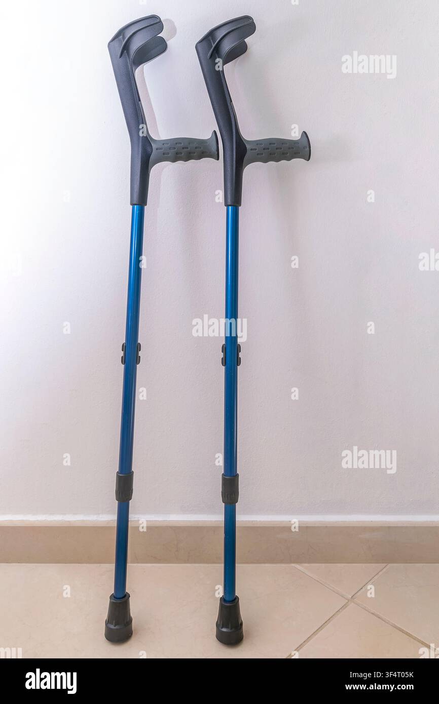 Une paire de béquilles bleues et noires s'appuie contre un mur blanc dans une maison Banque D'Images