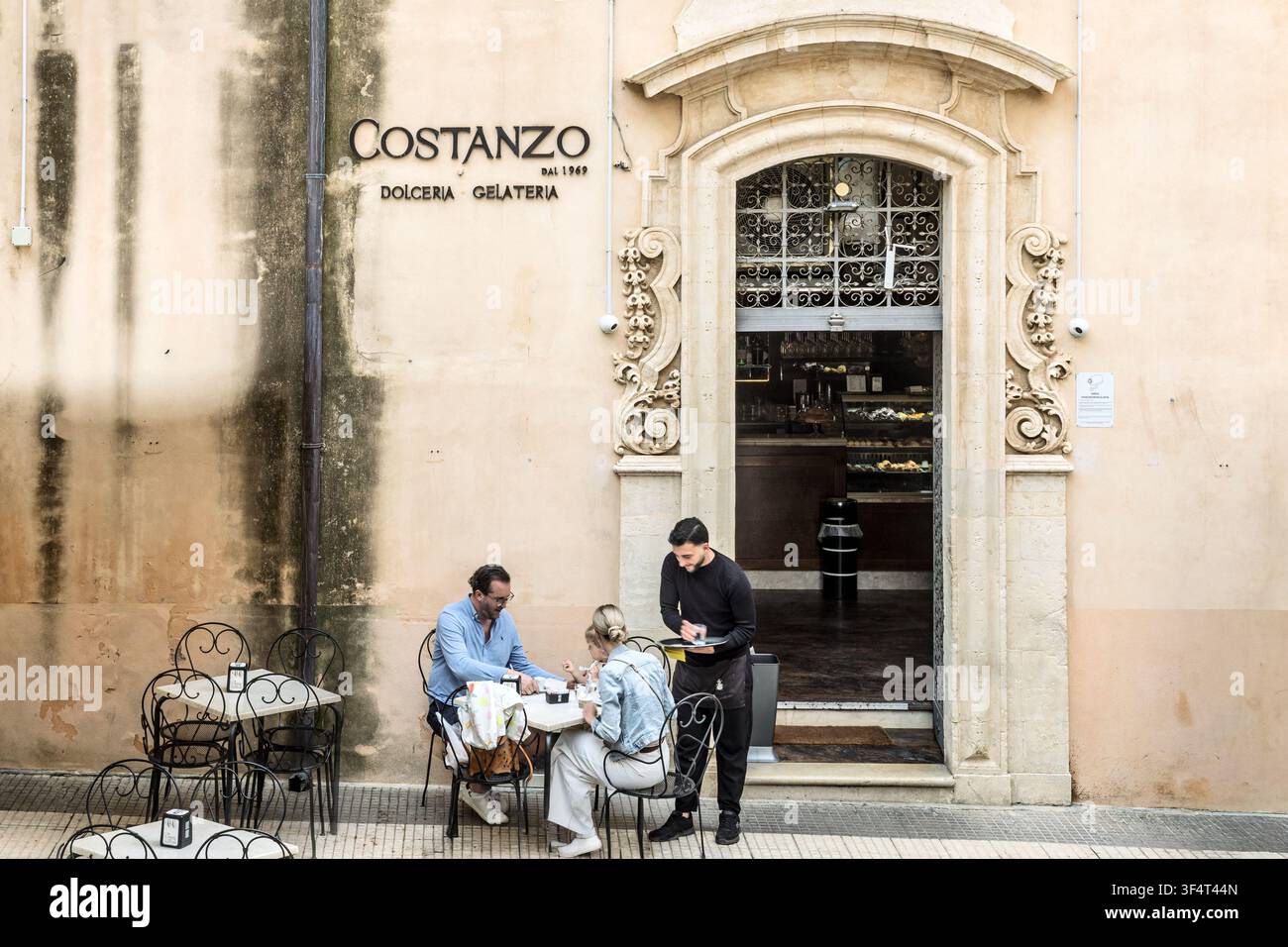 Serveur servant un couple à une table extérieure devant Costanzo, une dolceria & gelateria traditionnelle depuis 1969, Noto, Sicile, Italie Banque D'Images