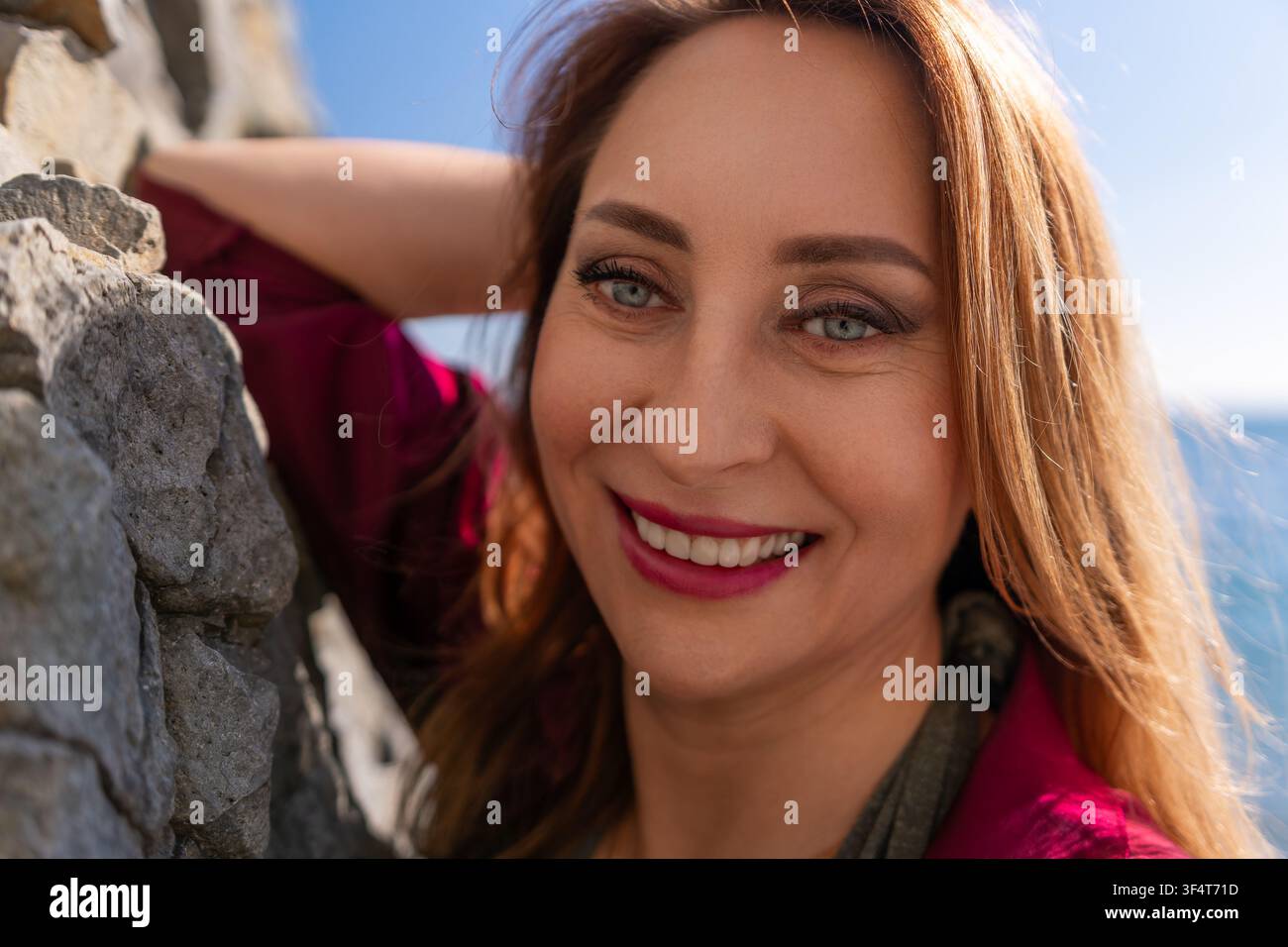 Femme souriante portrait belle femme adulte appuyée contre un mur de pierre en plein air par une journée ensoleillée profitant de ses vacances Banque D'Images