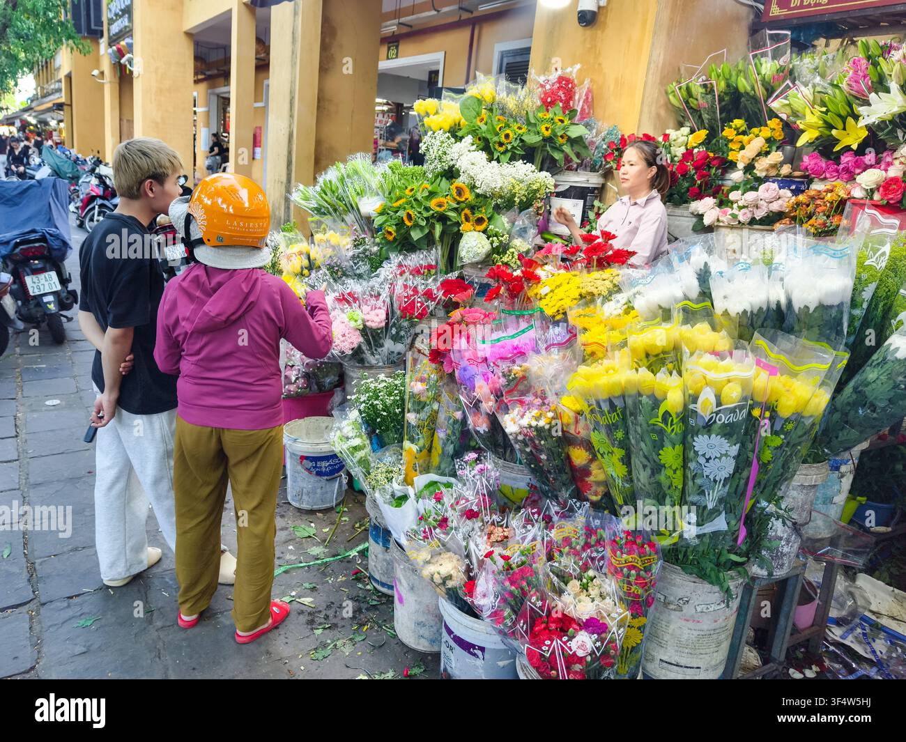 Étal de fleurs traditionnel à Hoi An, au Vietnam, présentant des présentations colorées de fleurs fraîches jaunes, rouges et blanches aux côtés de clients locaux et d’un vendeur. Banque D'Images