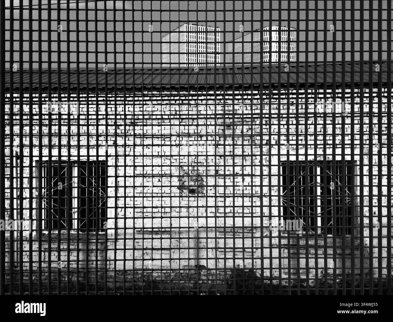 Un bâtiment industriel en brique est vu à travers une grille métallique dense qui crée des motifs superposés et une visibilité restreinte. Banque D'Images