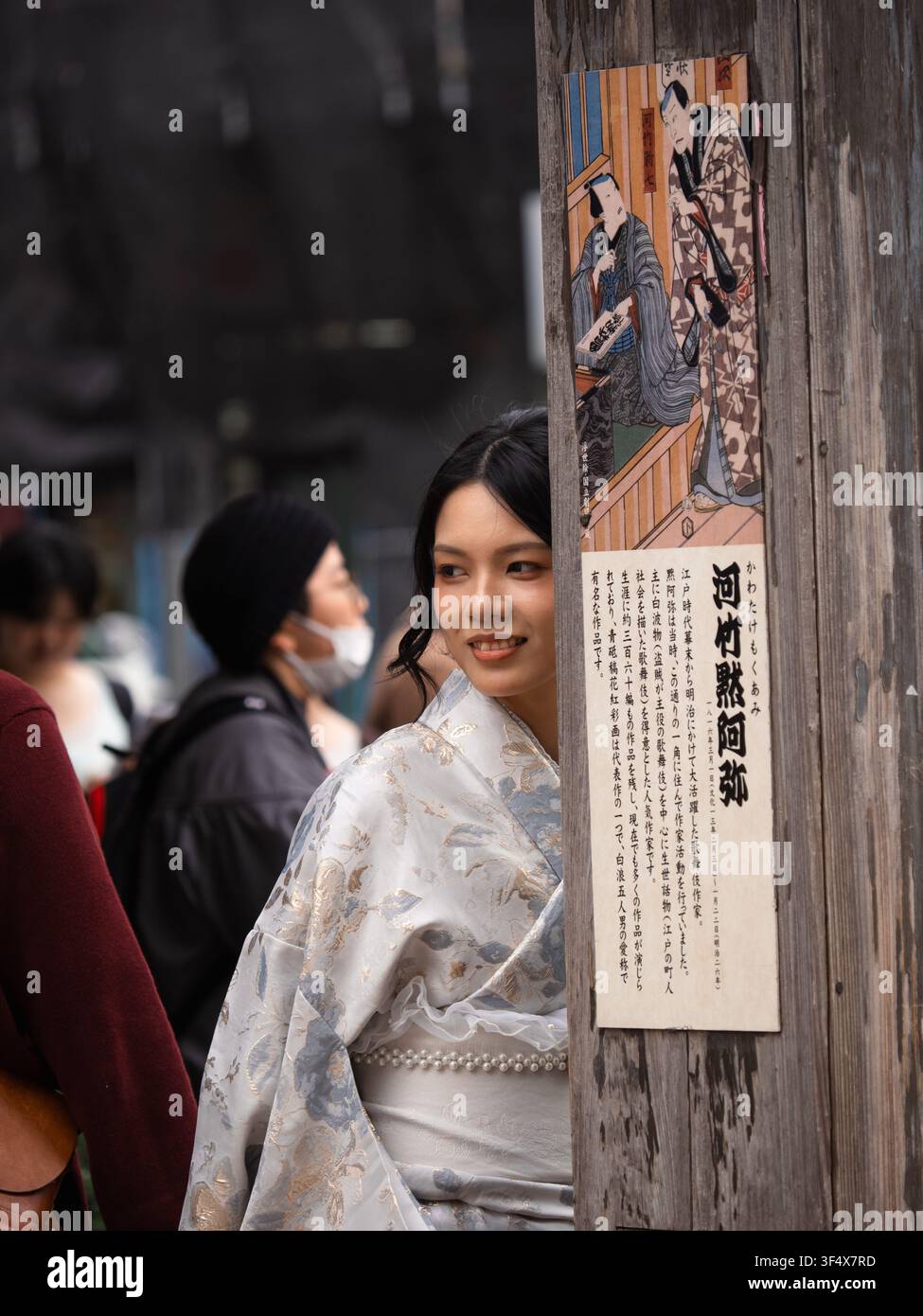 Jeune Japonaise en kimono blanc souriant à côté d'un poteau en bois orné d'une œuvre d'ukiyo-e près de Senso-ji, Asakusa, Tokyo Banque D'Images