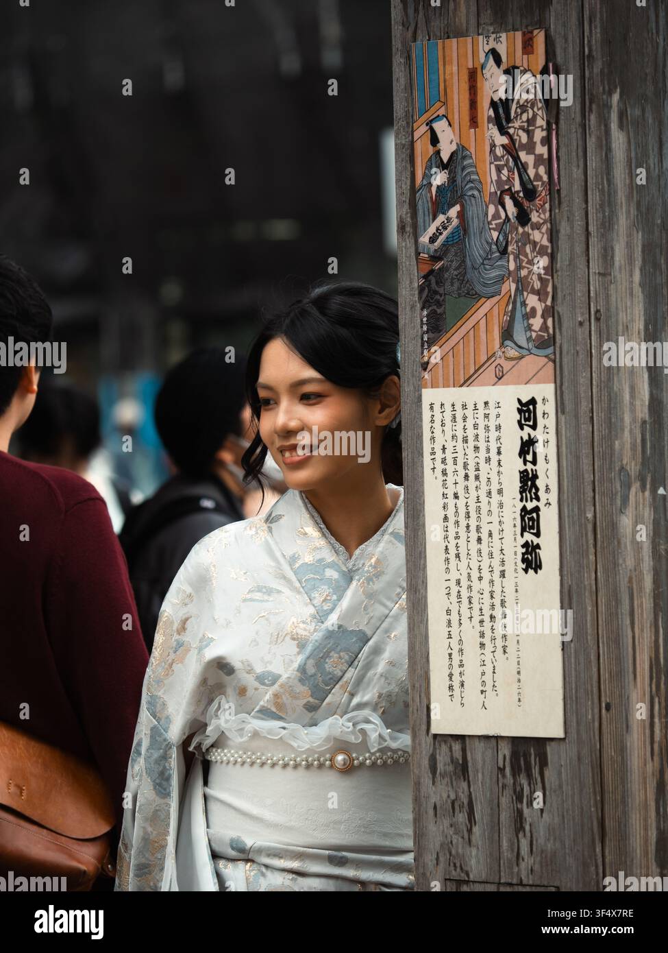 Jeune femme en kimono souriant près d'un poteau en bois avec une enseigne ukiyo-e à Asakusa, Tokyo, Japon Banque D'Images