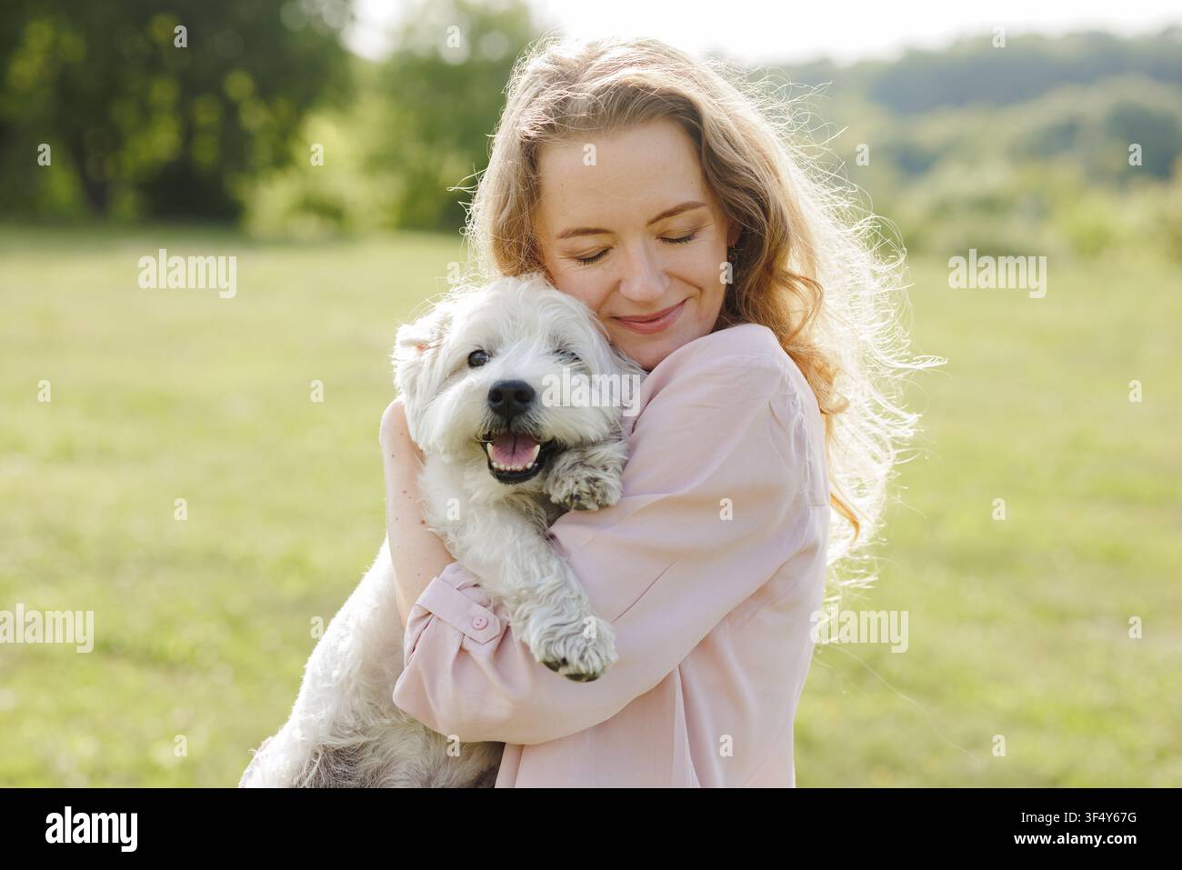 Une femme joyeuse caresse son chien heureux dans un parc ensoleillé, illustrant l'amour et les soins qui les lient, parfait pour les contenus et campagnes liés aux animaux de compagnie. Banque D'Images