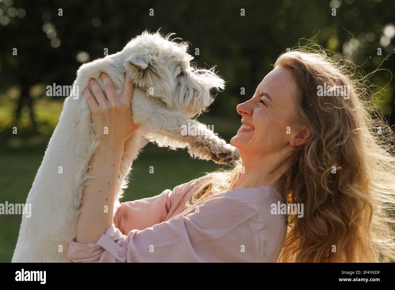 Une femme embrasse joyeusement son chien heureux dans un parc ensoleillé, mettant en valeur l'amour et le lien qui les unit, parfait pour les campagnes de soins aux animaux ou les moments réconfortants pe Banque D'Images