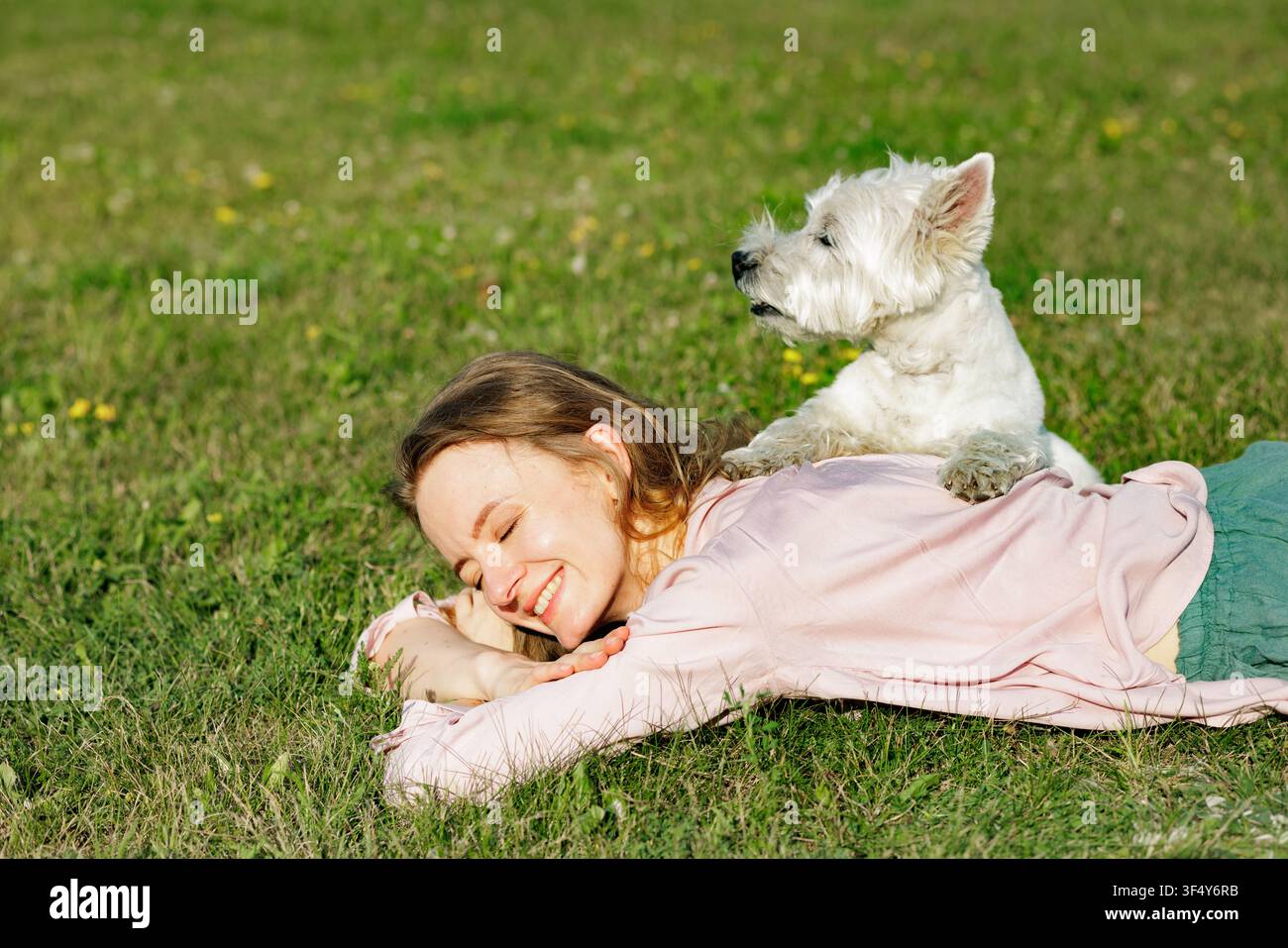 Une femme joyeuse est allongée sur l'herbe, souriant tandis que son chien heureux repose à ses côtés, illustrant l'amour et le lien qu'ils partagent dans un cadre de parc serein Banque D'Images