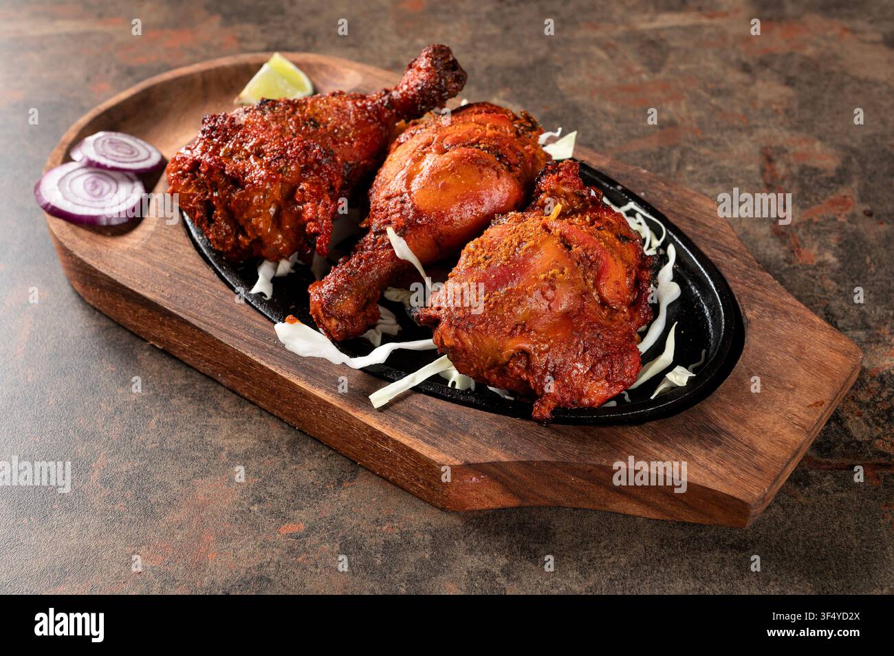 Poulet Tandoori servi sur un plat en fonte grésillant avec du chou, de l'oignon rouge et une tranche de citron vert sur une planche de service en bois. Grillé indien traditionnel c Banque D'Images