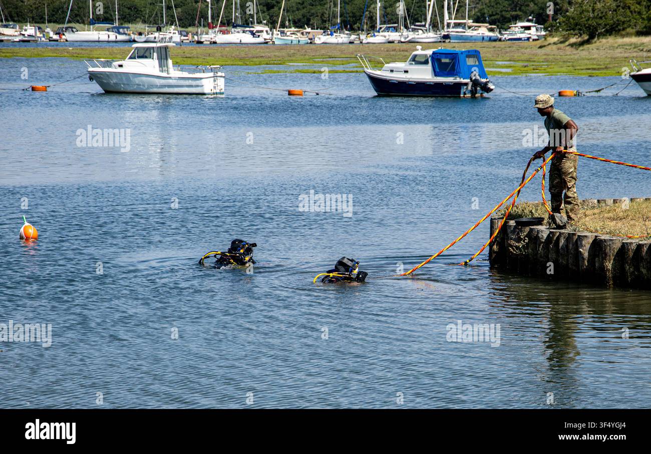 Deux plongeurs entrant dans les eaux estuariennes tandis qu'un homme sur le quai gère les cordes de plongée avec des bateaux amarrés en arrière-plan Bucklers Hard Hampshire Banque D'Images
