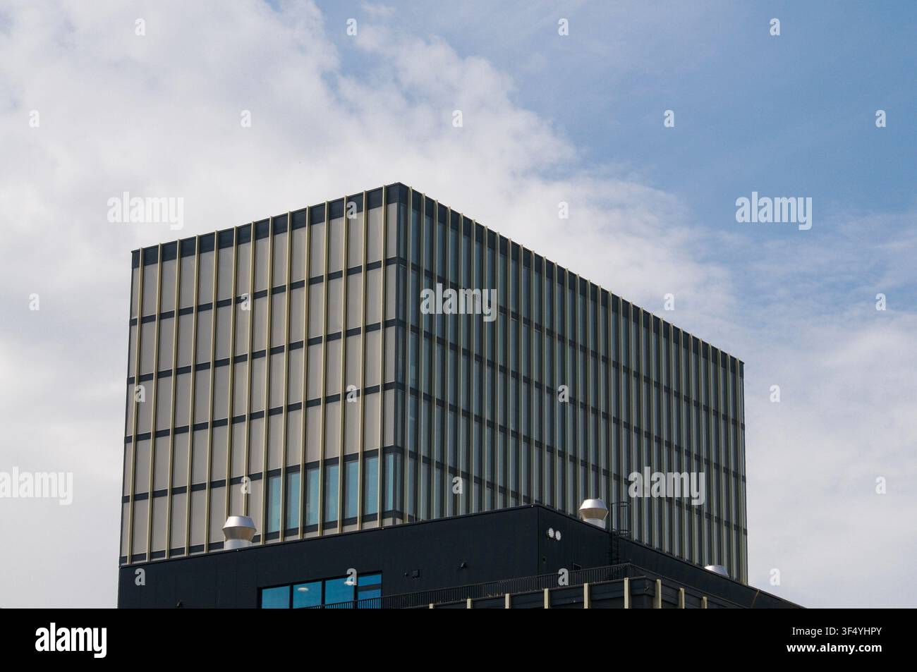 Vue en contre-plongée d'un bâtiment de bureaux moderne présentant une façade minimaliste avec des lamelles dorées verticales et une structure de grille géométrique sous un ciel bleu Banque D'Images