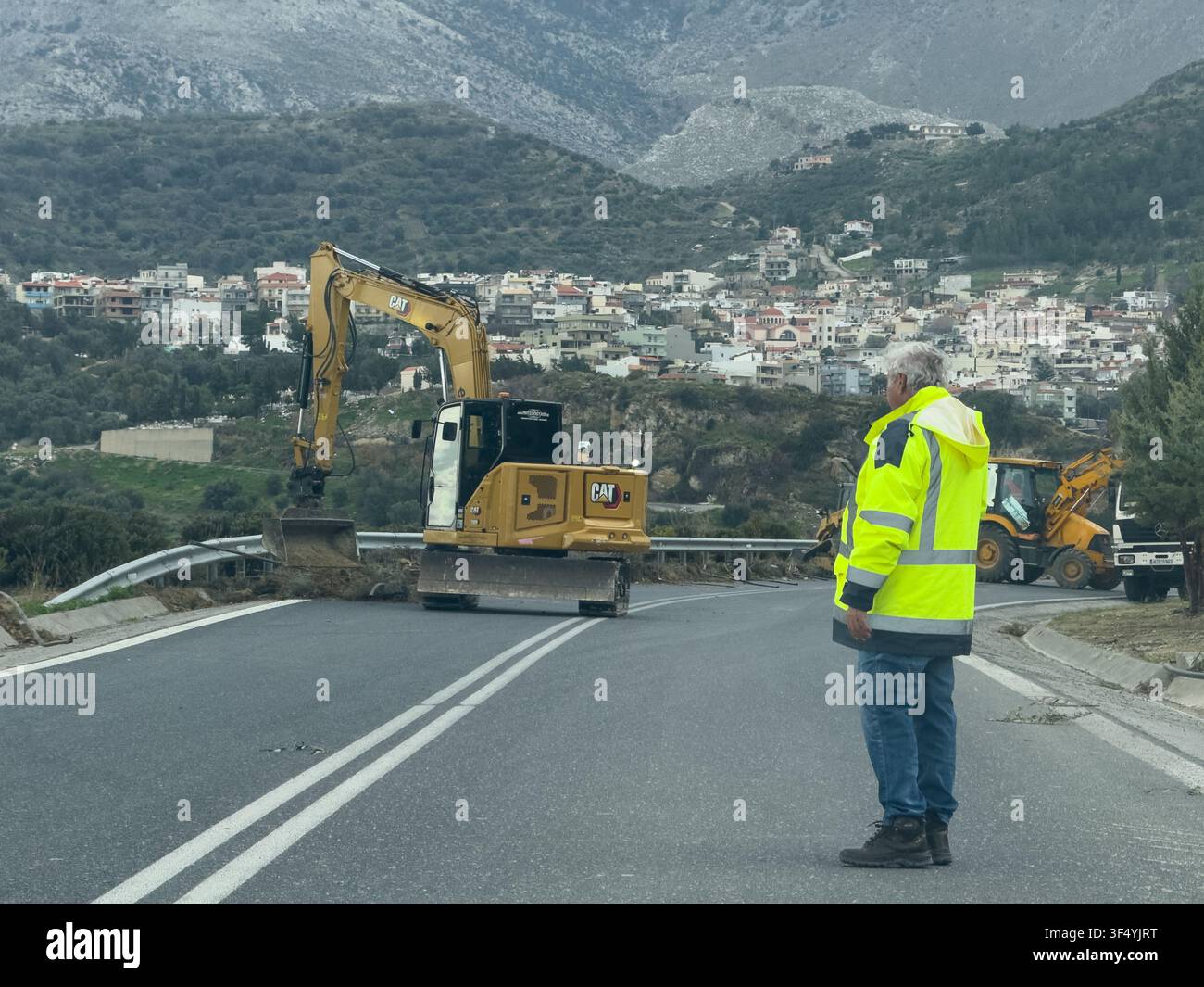 Ingénieur civil supervisant des travaux routiers avec des engins lourds et des montagnes en arrière-plan. Banque D'Images