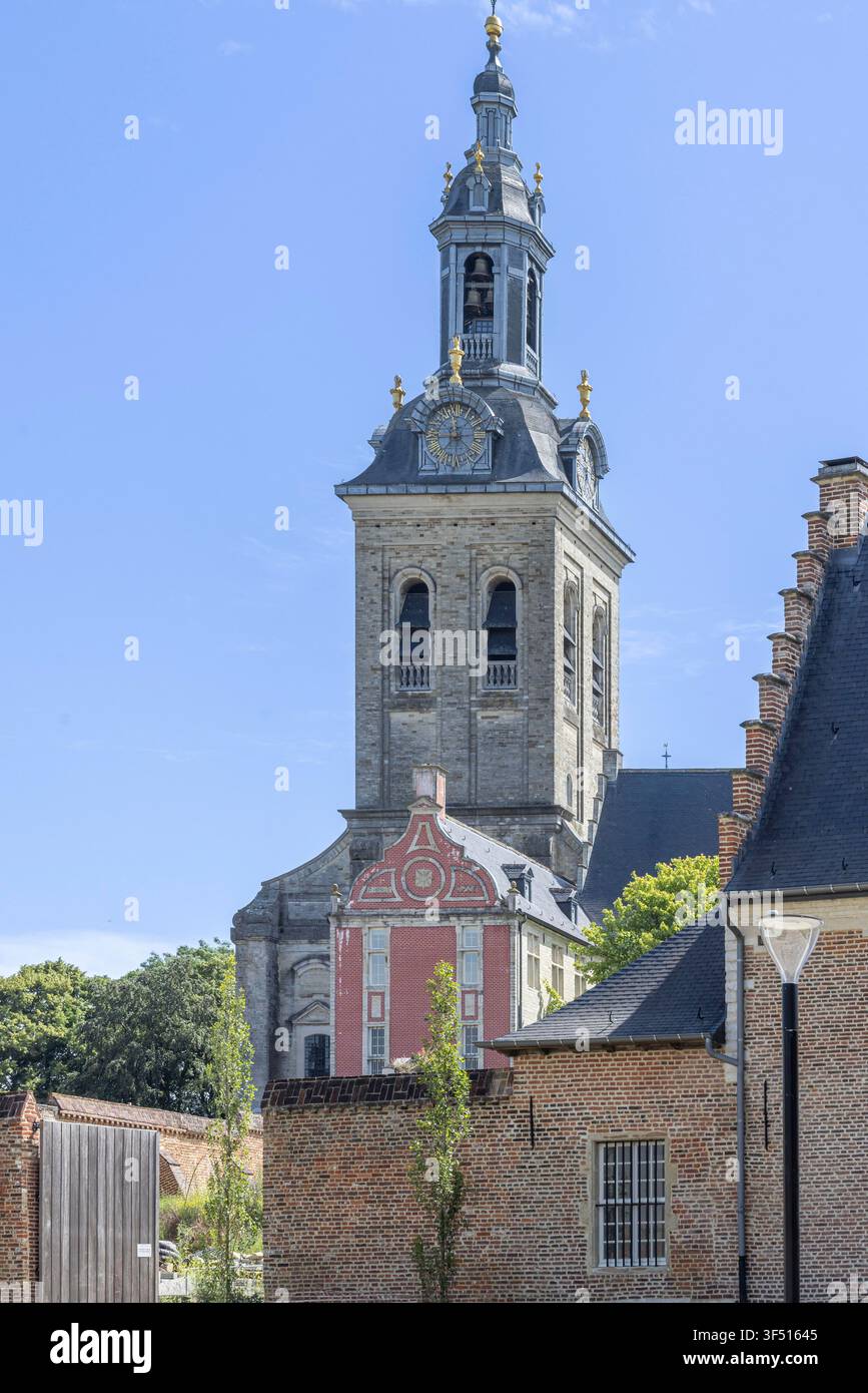 Le clocher historique de l'abbaye de Park s'élève au-dessus des bâtiments en briques rouges de Louvain, en Belgique, encadré par des arbres et un ciel bleu clair, mettant en valeur l'architecture baroque flamande et le charme urbain. Banque D'Images