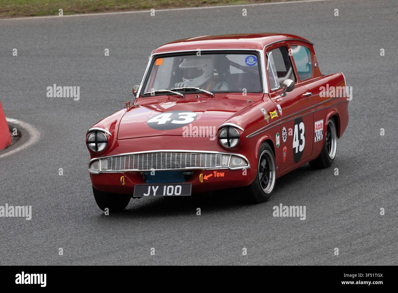 Une voiture de course historique Ford Anglia 105E rouge, portant le numéro 43 et l'immatriculation JY 100, naviguant sur une piste lors d'un événement de sport automobile classique Banque D'Images