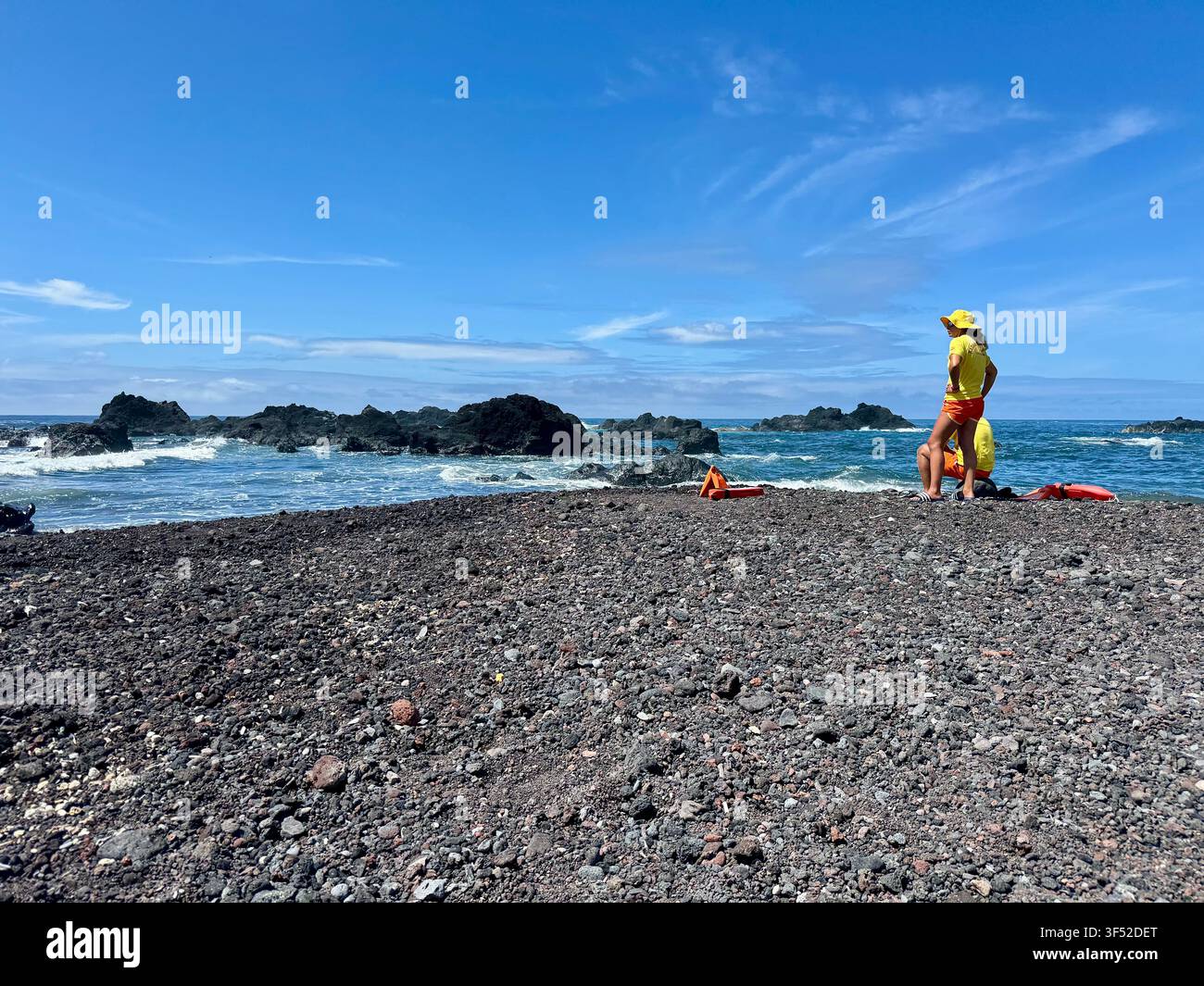Maîtres-nageurs en service sur la plage de galets volcaniques noirs et les bassins de baignade naturels de Mosteiros, île de São Miguel, Açores. - Image de stock capturée avec un smartphone