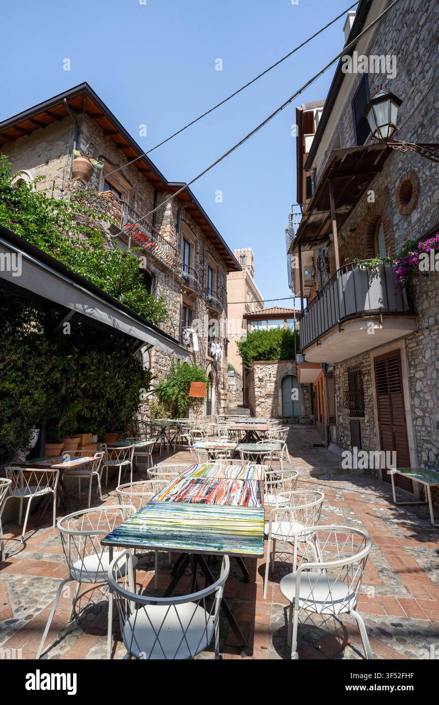 Tables de restaurant vides pour des repas en plein air entre des bâtiments historiques en pierre à Taormina, en Sicile Banque D'Images