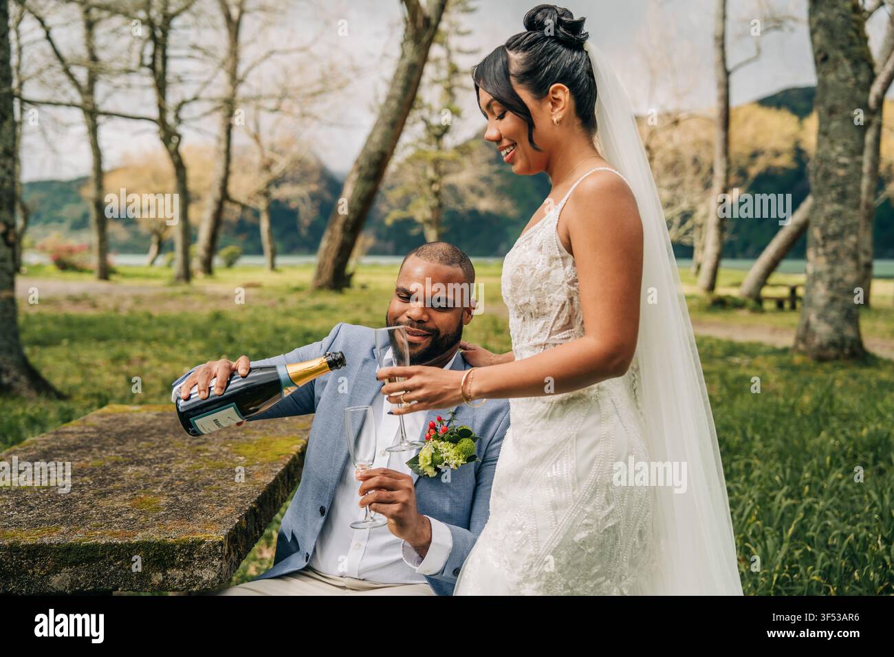 Couple de jeunes mariés heureux versant du champagne dans un parc Banque D'Images