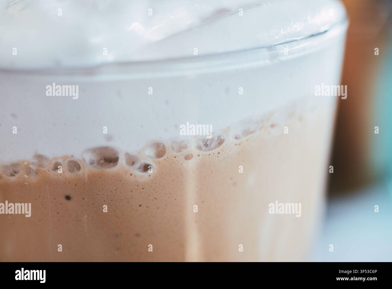 Vue macro d'une boisson froide au café dans un verre présentant des couches de liquide brun riche et un dessus de crème fouettée dense et mousseux, parfait pour les menus de café. Banque D'Images