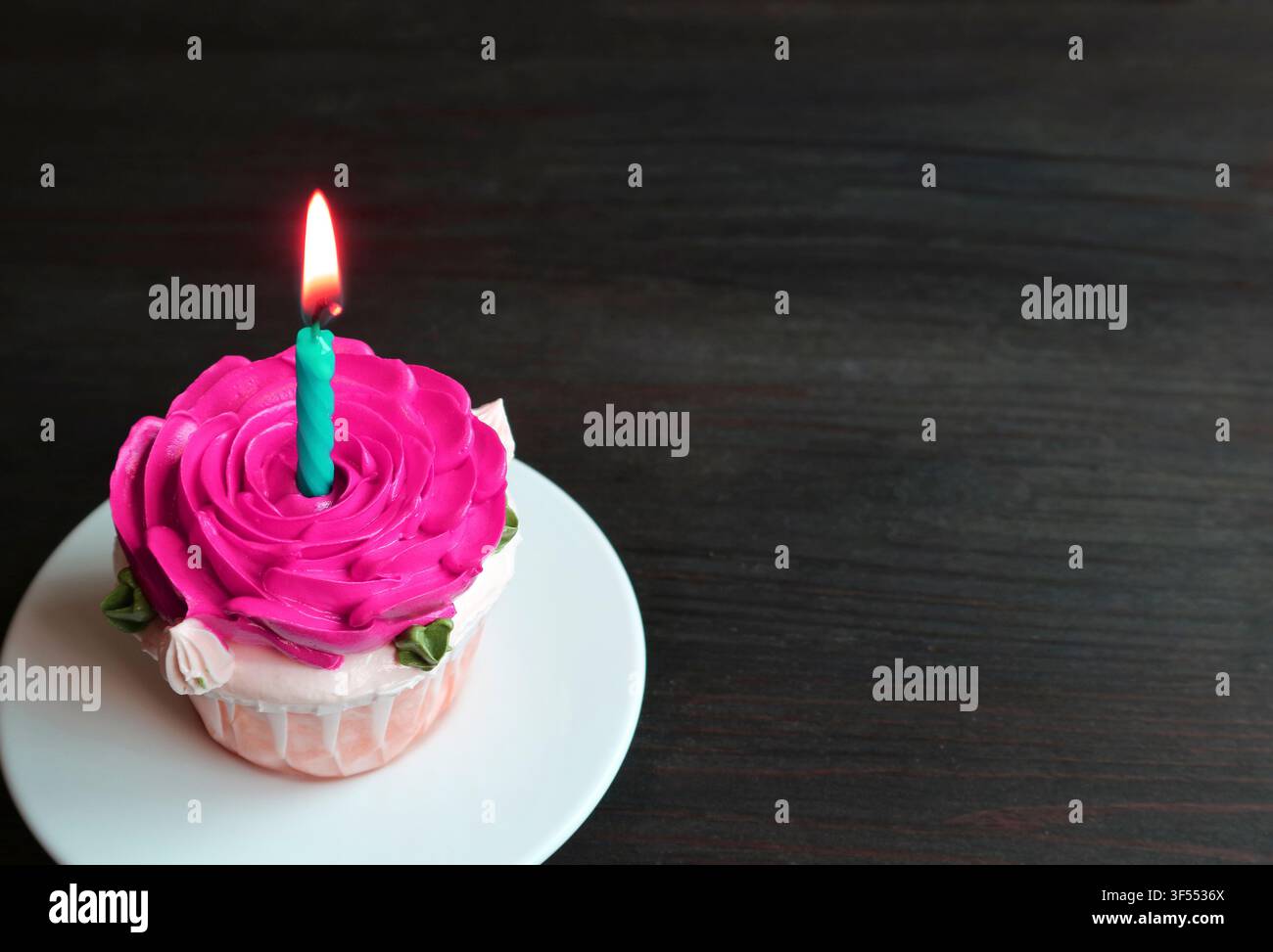 Beau gâteau d'anniversaire décoré avec une ganache rose vif en forme de rose et une bougie brillante allumée Banque D'Images