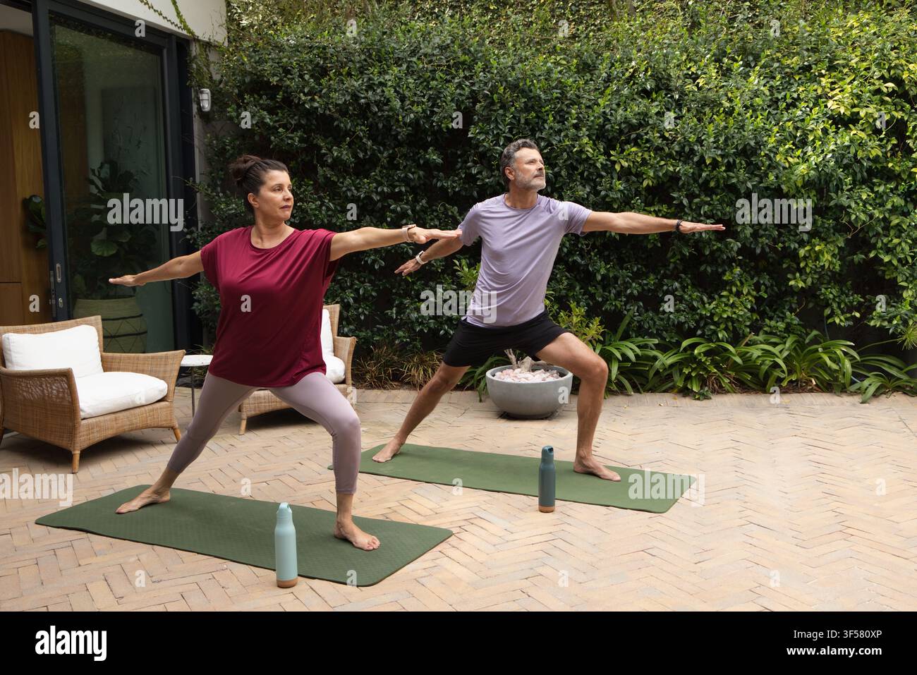 Couple divers pratiquant le yoga debout sur des tapis verts sur une terrasse en chevrons avec des bouteilles d'eau Banque D'Images
