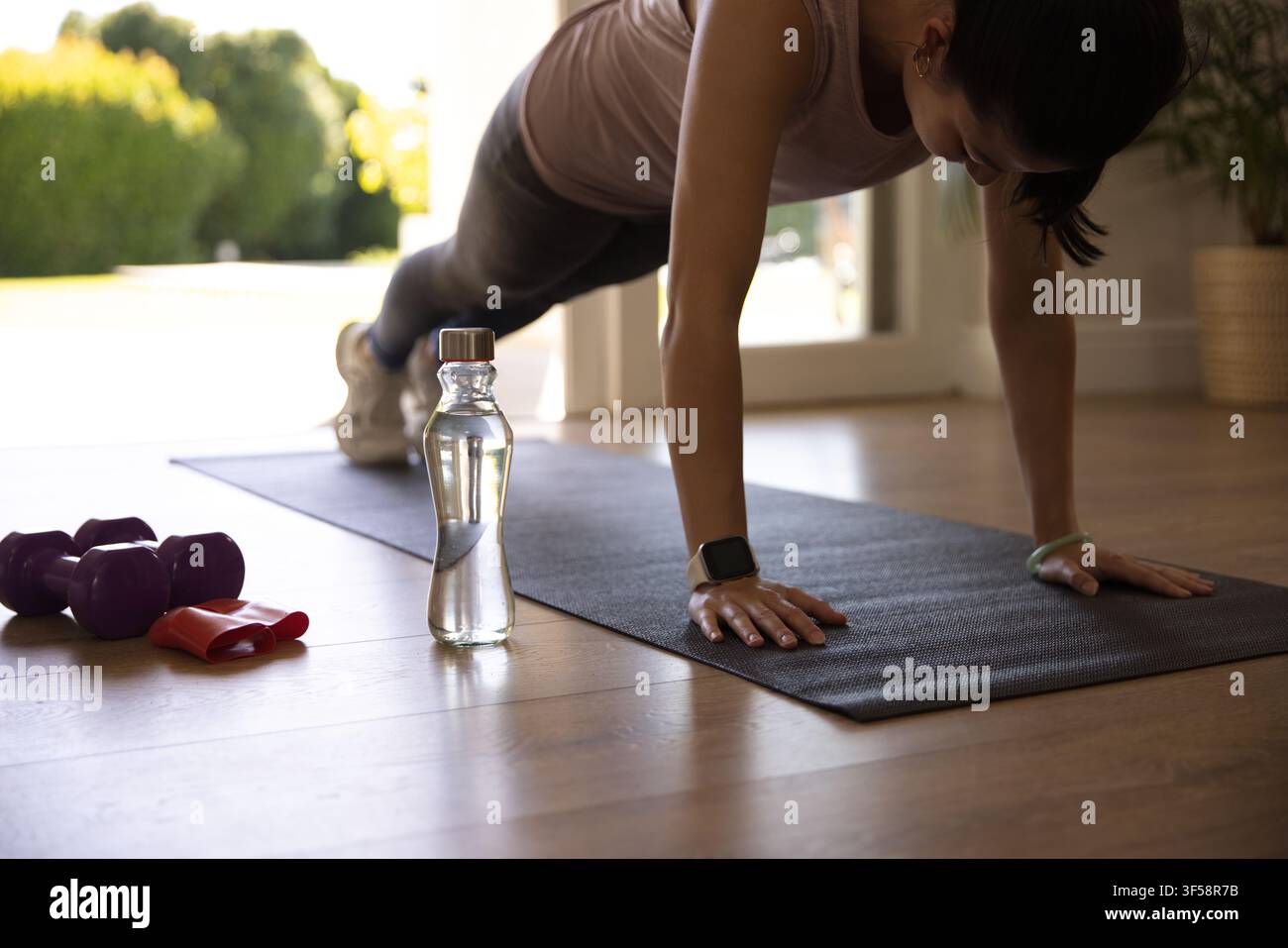Femme afro-américaine effectuant un plank sur un tapis près d'une porte coulissante, portant un débardeur et un legging Banque D'Images