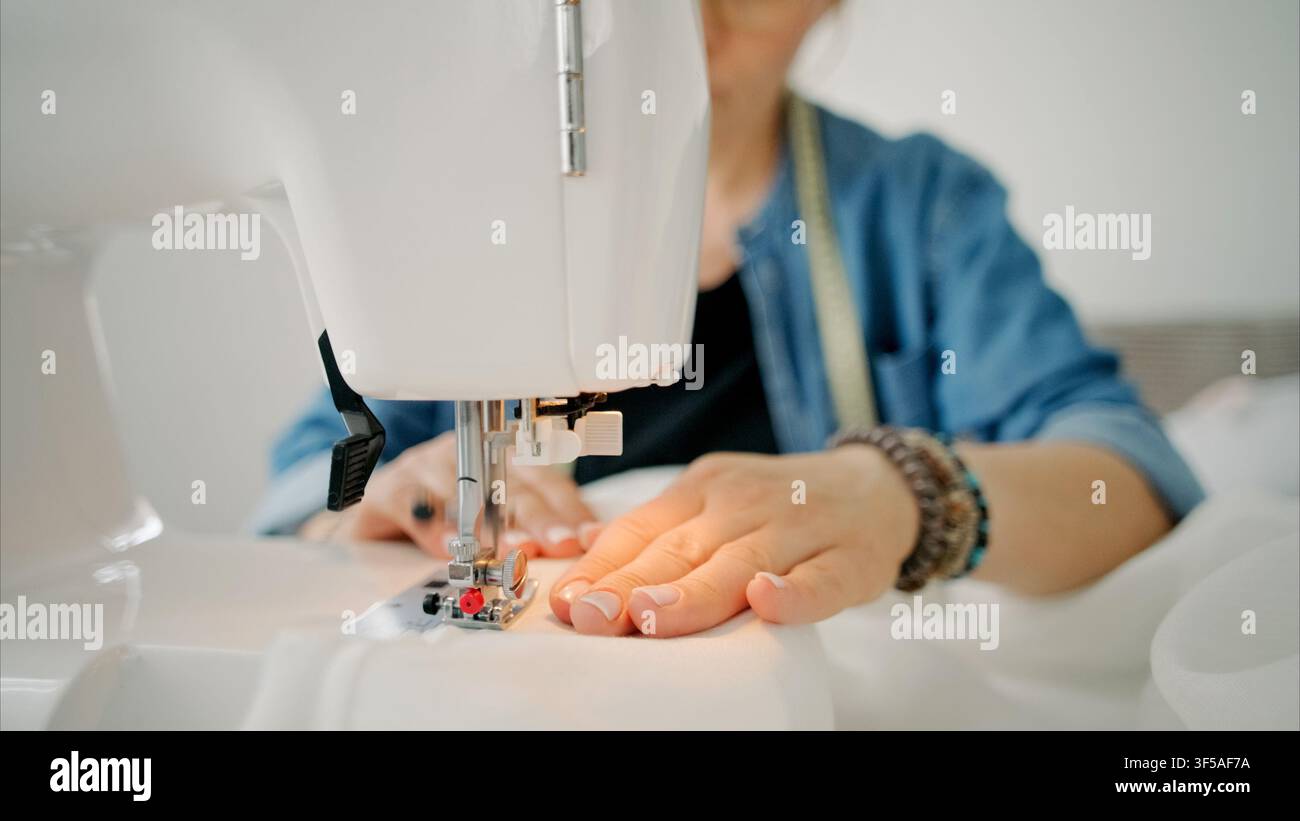 Une personne guide soigneusement un tissu blanc à travers une machine à coudre moderne lors d'un projet créatif Banque D'Images