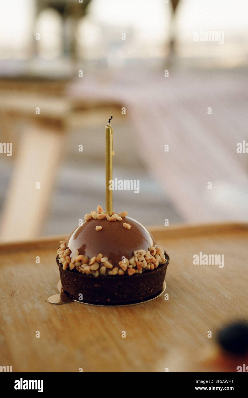 Gâteau dôme en mousse au chocolat unique avec une bougie dorée au sommet, préparé pour une célébration d'anniversaire. La scène met en valeur un dessert festif dans une atmosphère chaleureuse et élégante Banque D'Images
