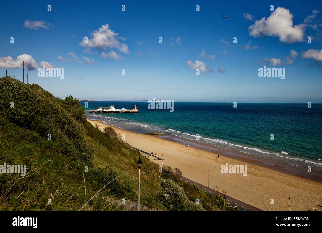 Une large plage de sable au pied de falaises abruptes avec une jetée s'avançant dans une mer bleu profond, Bournemouth, Dorset, Angleterre. Banque D'Images