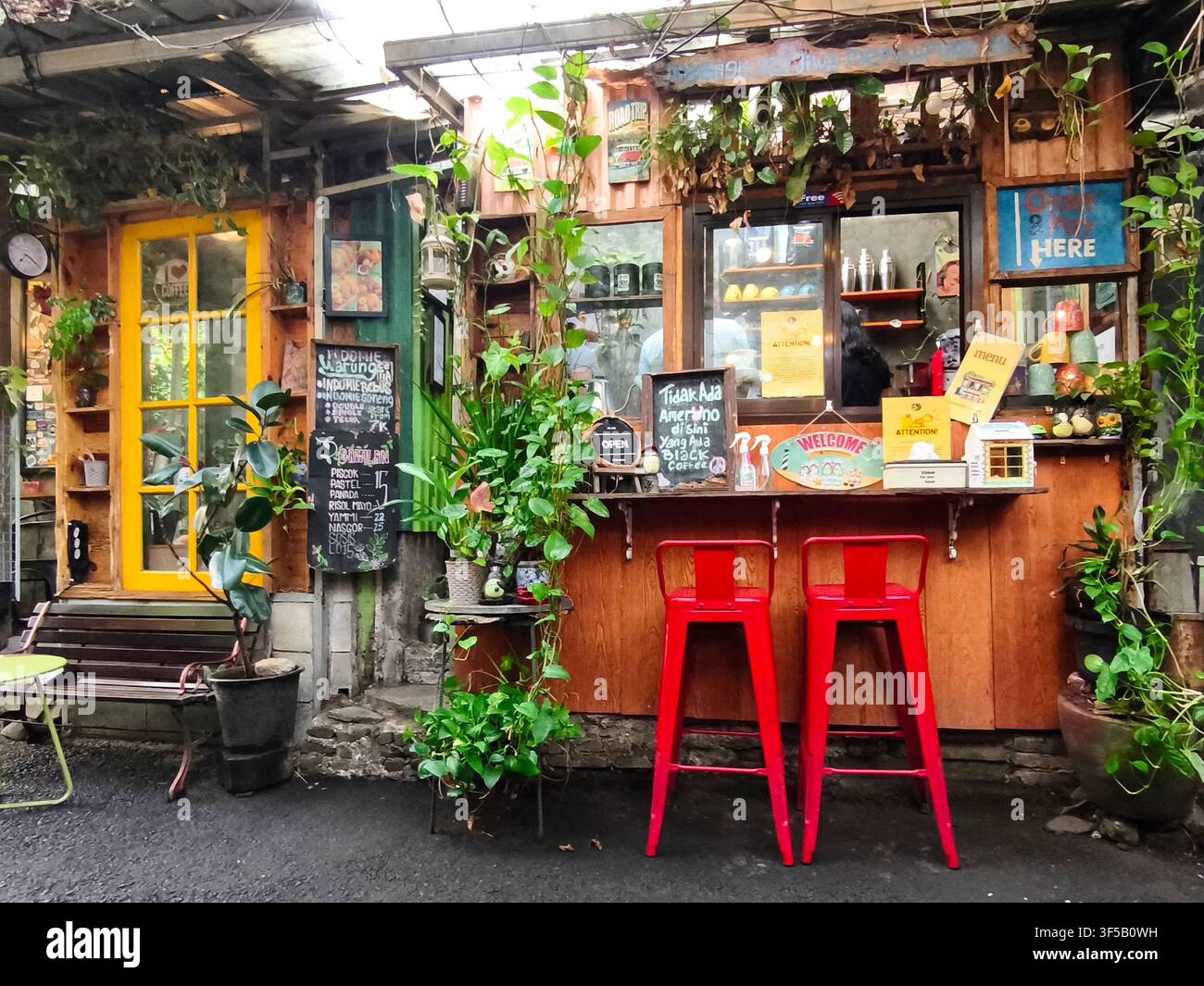 Un kiosque à café rustique et confortable entouré d'une végétation luxuriante, avec des détails en bois chaleureux, une décoration colorée et des tabourets rouges vifs Banque D'Images