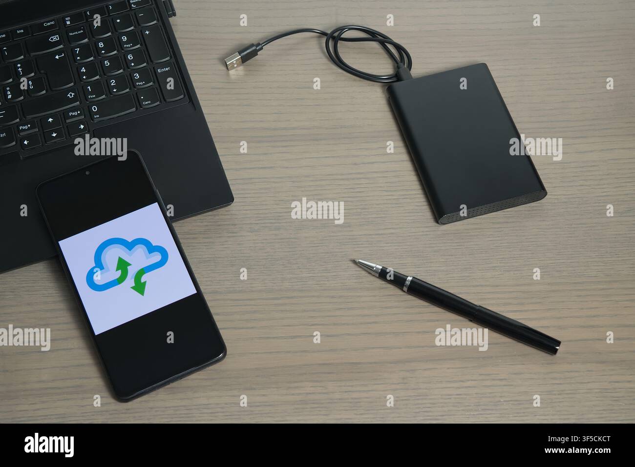 Une disposition de bureau avec un ordinateur portable, un dispositif de stockage externe, un stylo et un smartphone affichant la synchronisation cloud. Banque D'Images