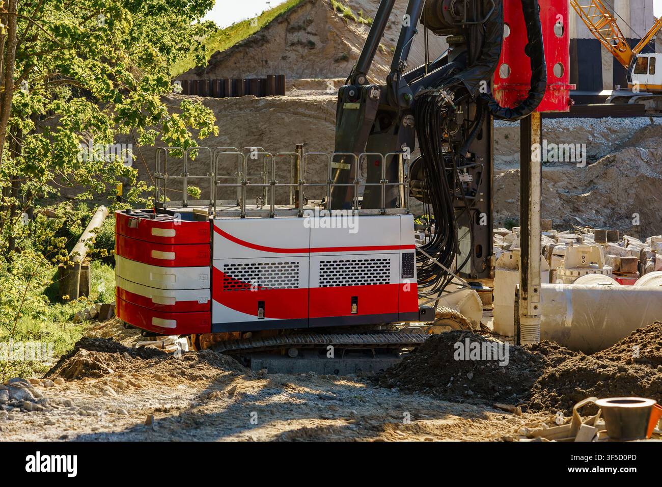 Machine de forage industriel en activité sur un chantier ensoleillé avec un sol en terre et gravier, ingénierie géotechnique, forages de fondations profondes, opérations de machines lourdes, infrastructures Banque D'Images