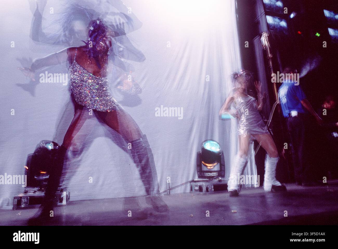 DANSEURS EN PERFORMANCE SUR SCÈNE AVEC EFFET DE FLOU DE MOUVEMENT, FESTIVAL HOMELANDS 2001, SCÈNES DE FOULE ET DANSE, WINCHESTER, ANGLETERRE, 2001 : Deux danseuses en tenues argentées et blanches étincelantes se produisent sur une scène brillamment éclairée, avec un effet de flou de mouvement capturant l'énergie de la danseuse principale. Scènes de foule, atmosphère et danseurs du Festival Homelands, Winchester Bowl, Angleterre, le 25 mai 2001. Photo : Rob Watkins. INFO : Le Festival Homelands était un festival de musique dance pionnier au Royaume-Uni célébrant la house, la trance et la musique électronique. Il a attiré les DJ leaders et des milliers de fans à la fin des années 1990 et au début des années 2000. Banque D'Images
