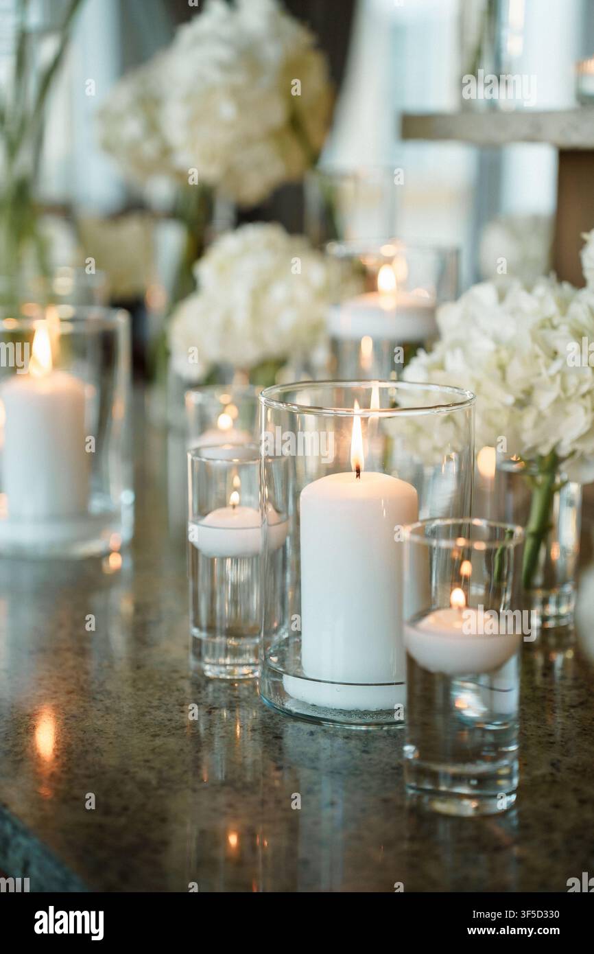 Close up d'une décoration de table de mariage mettant en vedette des bougies piliers allumées dans des cylindres en verre entrecoupées de somptueuses fleurs d'hortensia blanches pour une décoration romantique de soirée, idéale pour une décoration de mariage ou d'événement formel Banque D'Images