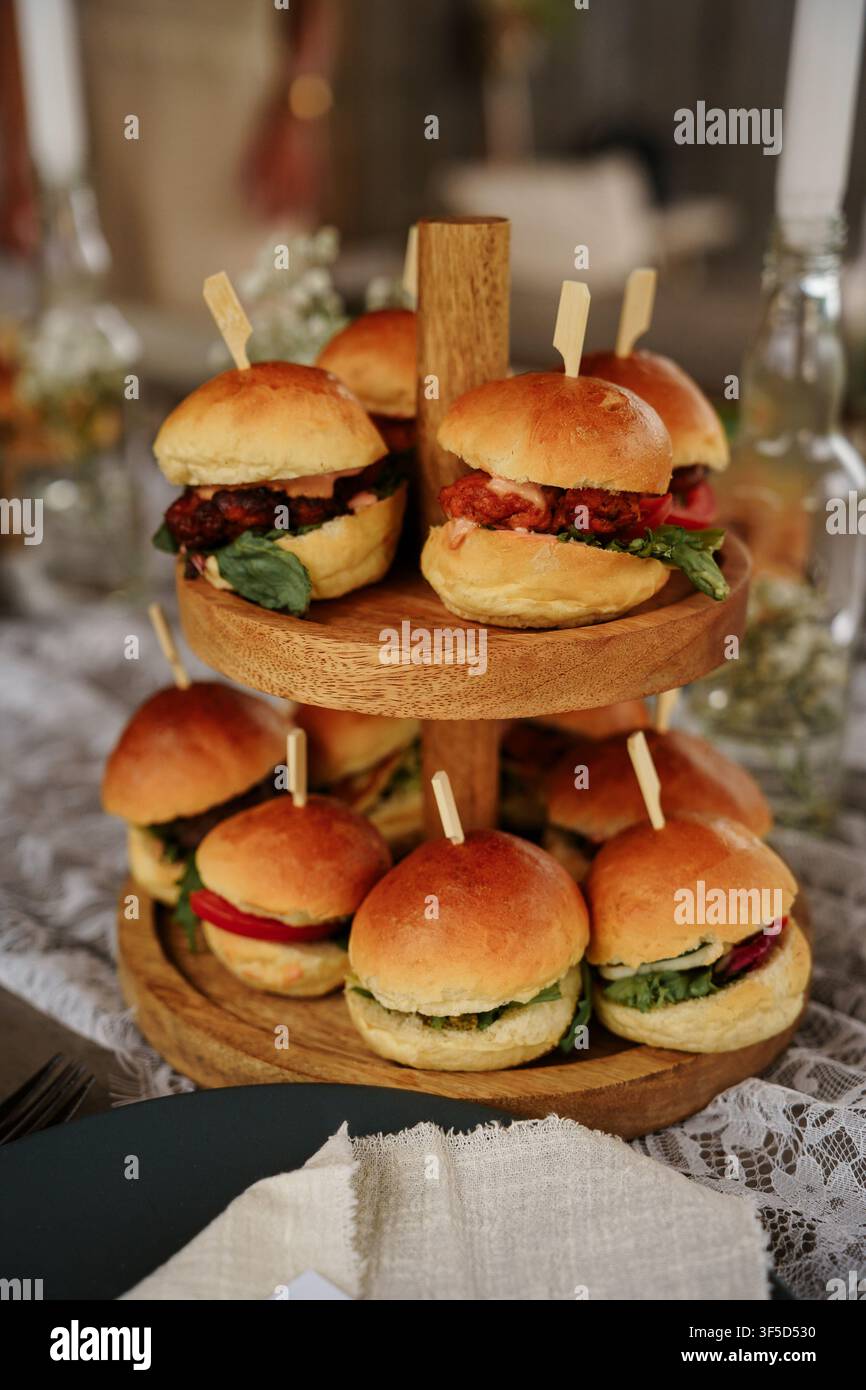Plateau en bois rustique à deux niveaux rempli de mini burgers gastronomiques, parfait pour un catering de mariage élégant, des amuse-gueules de fête ou des présentations de plats de restaurant Banque D'Images