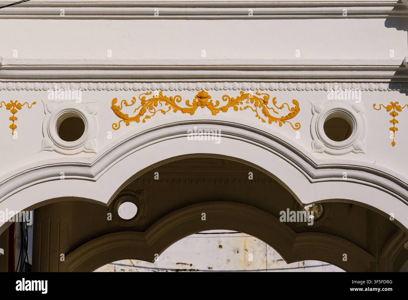 Close-up élégant d'une arche coloniale décorative avec des moulures en plâtre classiques, des motifs ornementaux et des ouvertures circulaires sur un bungalow historique Banque D'Images