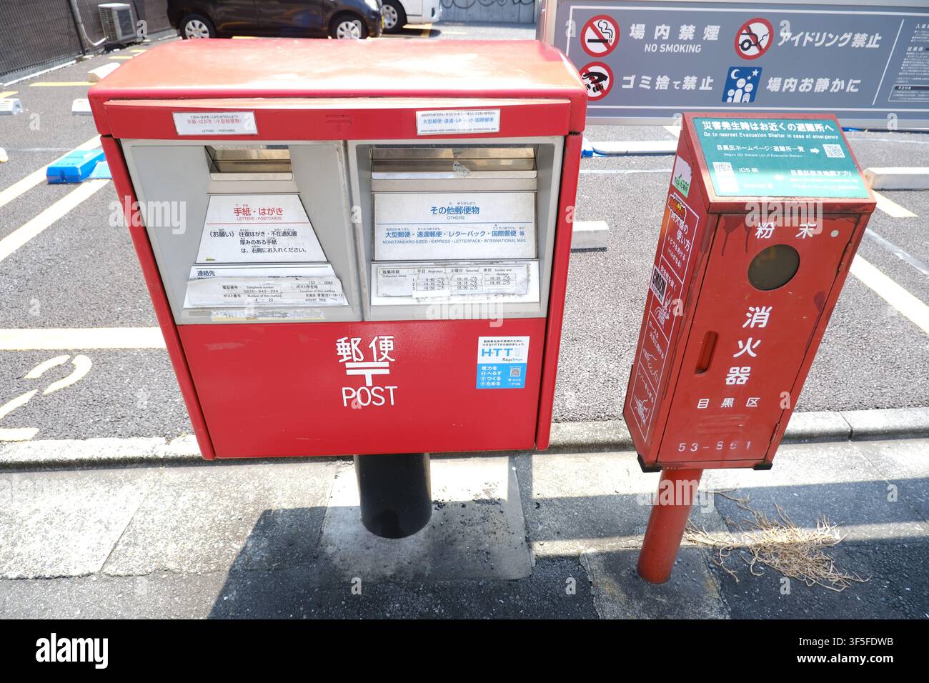 Une boîte postale japonaise rouge se trouve à côté d'une boîte d'extincteur rouge sur un trottoir pavé à Meguro City, Tokyo, Japon. Banque D'Images
