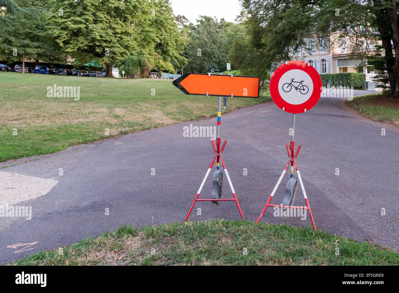 Une flèche de direction orange portable et un panneau d'interdiction de vélo bloquent un chemin pavé, indiquant un détour temporaire ou une restriction d'accès. Banque D'Images