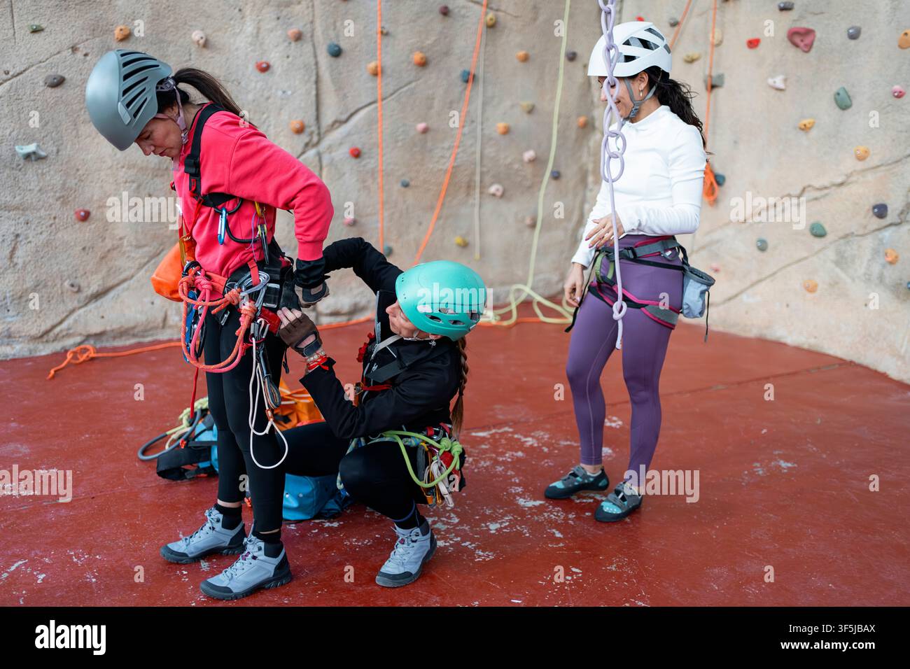 Trois femmes préparent des harnais et des cordes de sécurité sur un mur d'escalade intérieur, pratiquant l'exploration spéléologique et les techniques d'entraînement vertical avec casques et protection Banque D'Images