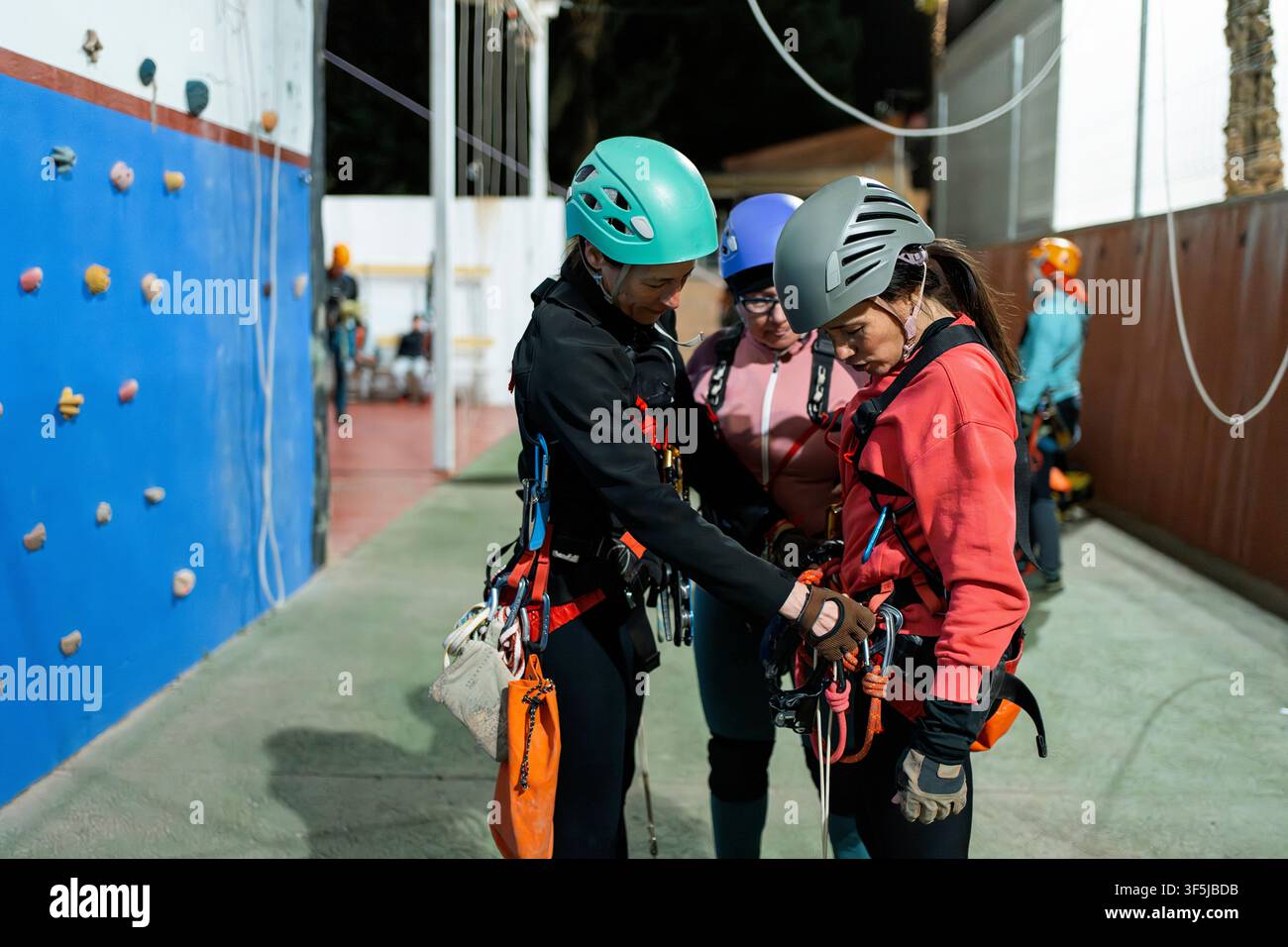 Trois femmes portant des casques et des harnais préparent l'équipement d'escalade lors d'un entraînement de spéléologie verticale dans une salle de gym intérieure, pratiquant l'accès par corde et la sécurité Banque D'Images