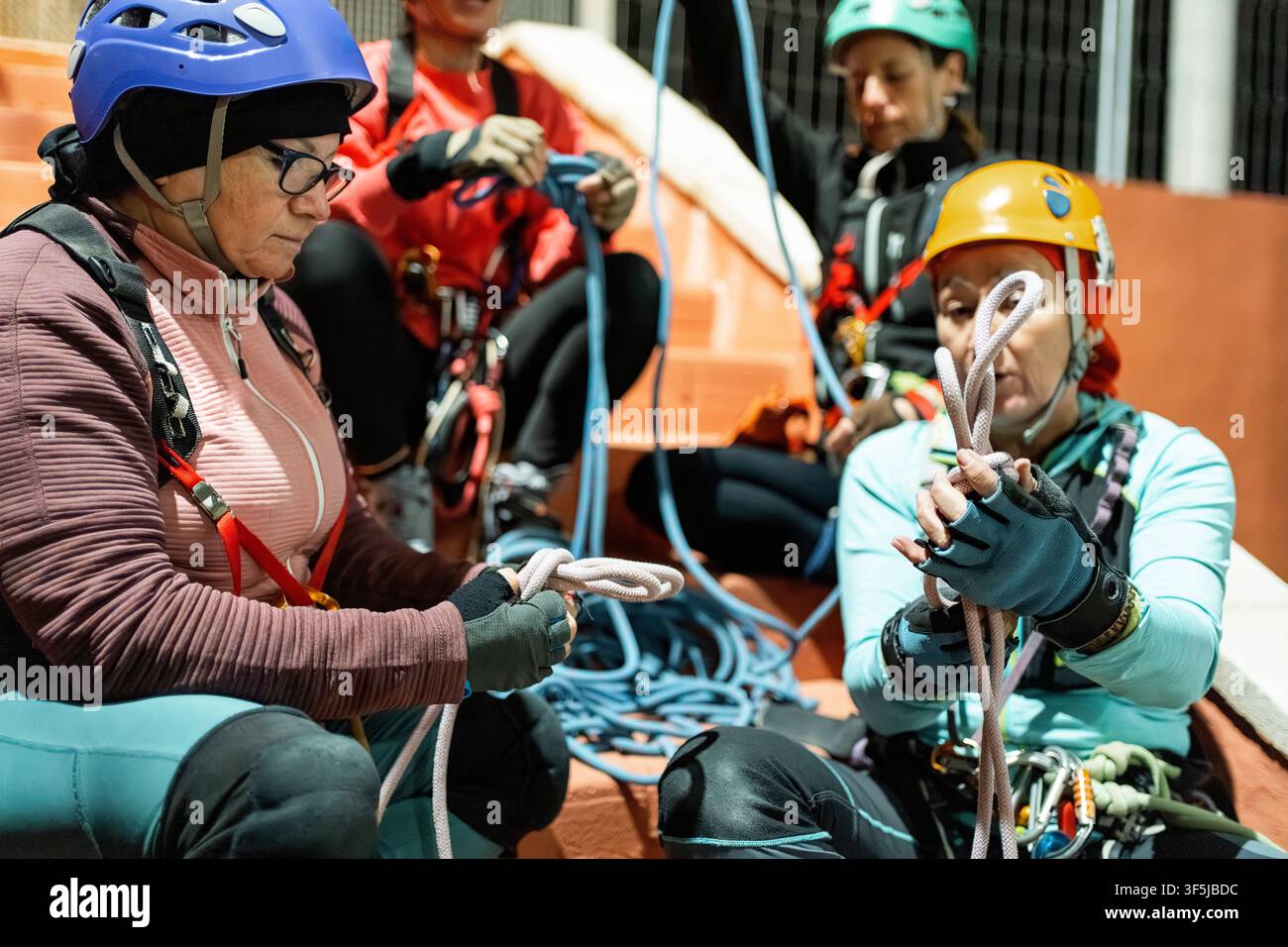 Des femmes portant des casques et des harnais pratiquent les nœuds de corde et les techniques de spéléo verticales lors d'une séance d'entraînement en salle avec un équipement de sécurité. Banque D'Images