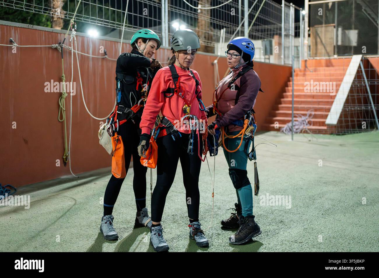 Trois femmes portent des casques, des harnais et un équipement d'escalade alors qu'elles se préparent à un entraînement de spéléo verticale dans une salle de sport en plein air, pratiquant l'accès par corde et la sécurité Banque D'Images