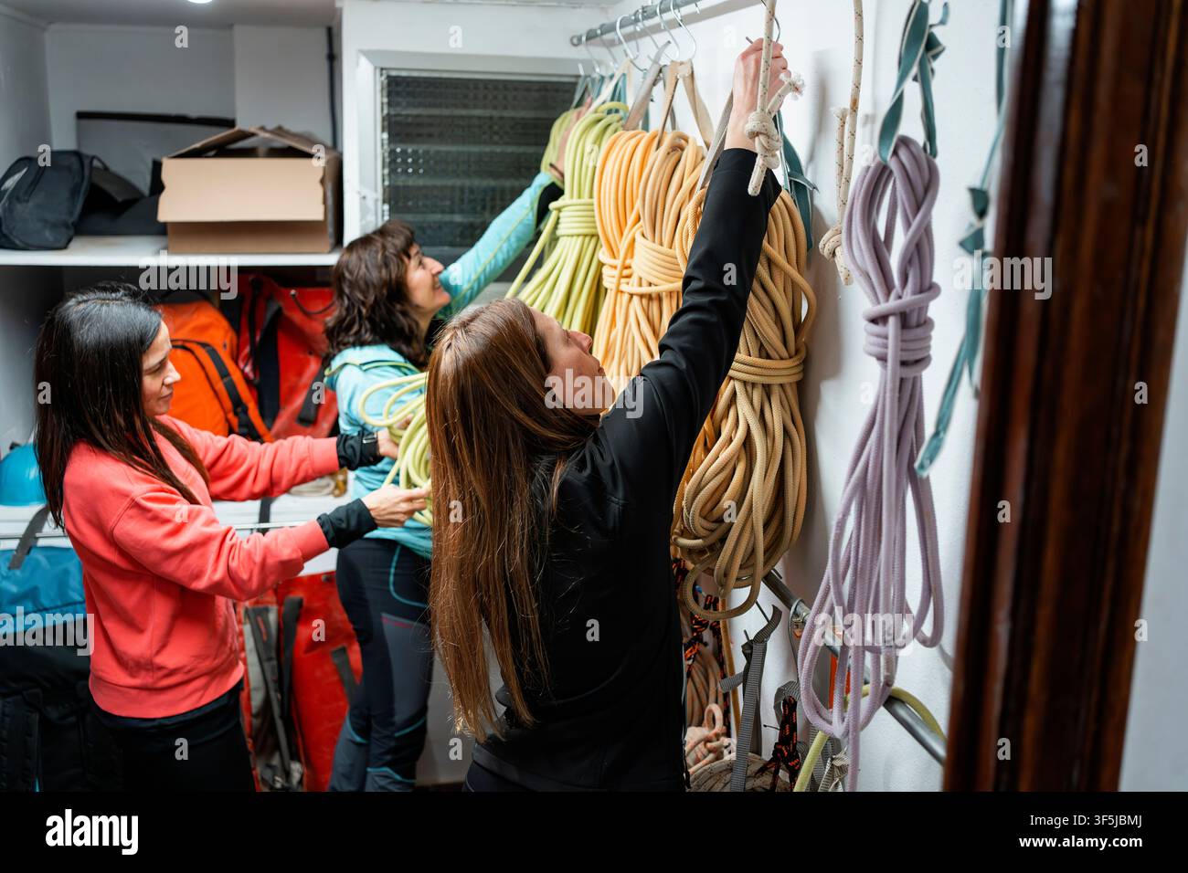 Trois femmes organisent des cordes et de l'équipement de sécurité dans un débarras de salle de sport après une session d'entraînement spéléo vertical, préparant du matériel d'escalade pour la prochaine u Banque D'Images