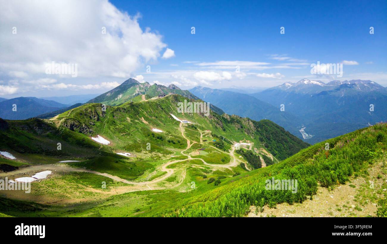 Une vue panoramique d'une chaîne de montagnes verdoyante pendant l'été sous un ciel bleu éclatant parsemé de nuages blancs. Des routes de terre sinueuses et des sentiers traversent t Banque D'Images