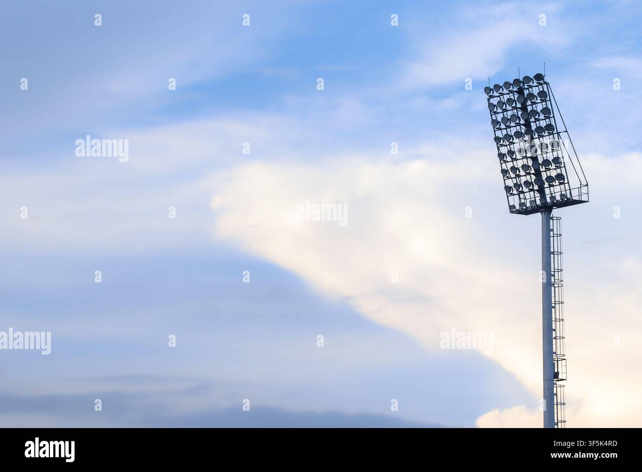 Tour de projecteurs du stade contre un ciel bleu et des nuages blancs, montrant l'infrastructure du stade et l'éclairage pour les événements en plein air. Banque D'Images