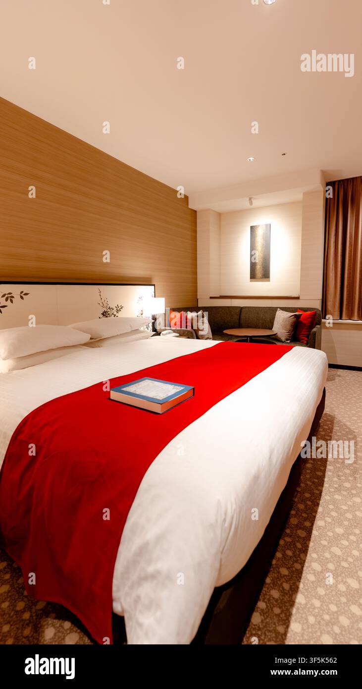 Une chambre d'hôtel moderne à Tokyo dotée d'un lit moelleux avec des accents rouges, d'une décoration élégante et d'un éclairage d'ambiance, créant une atmosphère chaleureuse et accueillante pour Banque D'Images