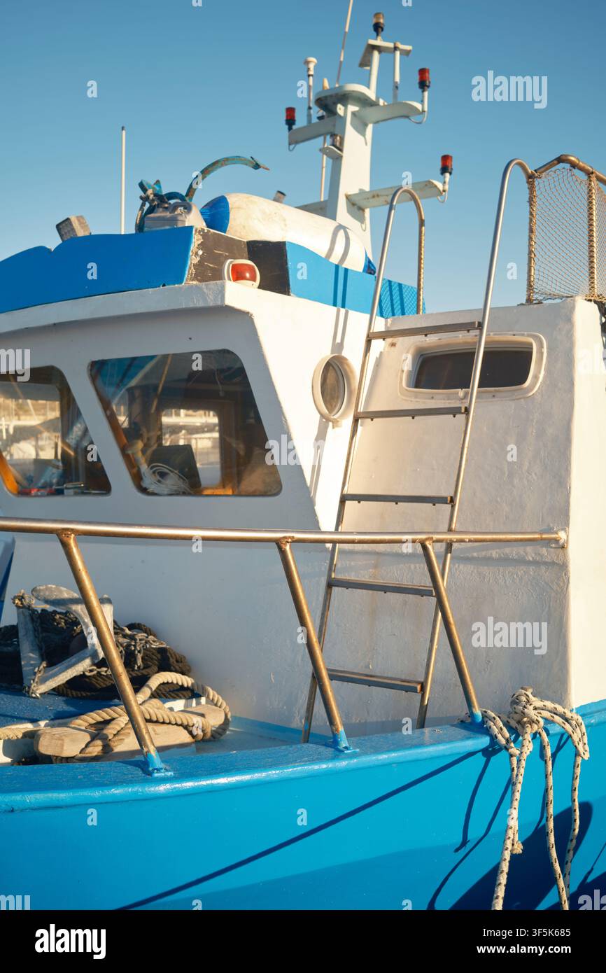 Close-up d'équipement de bateau de pêche bleu et blanc usé, corde enroulée, rampes métalliques et filets sous un soleil chaud à Favignana, Sicile, Italie, wit Banque D'Images