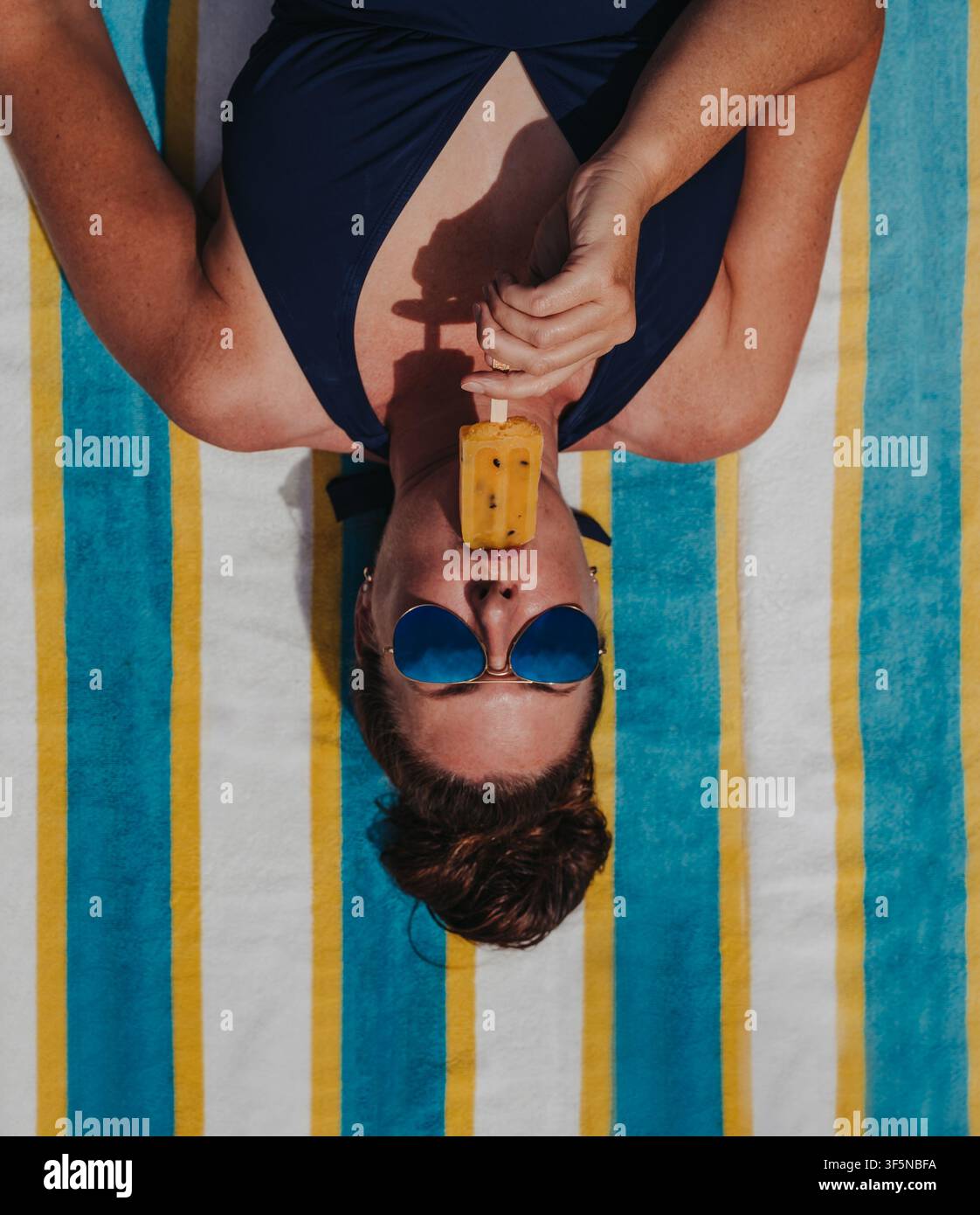 Femme savourant une glace à l'eau sur une serviette rayée vue du dessus Banque D'Images