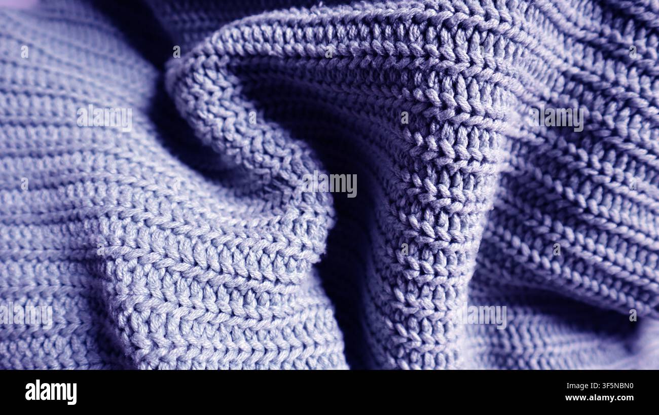 Une vue rapprochée d'un tissu tricoté violet avec des plis doux. La texture montre le design complexe du tricot. Une ambiance douillette se dégage à travers le mate Banque D'Images
