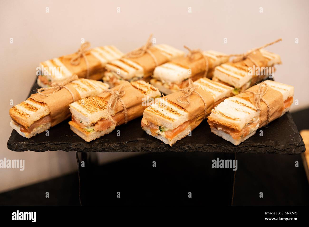 Sandwiches grillés enveloppés dans du papier sur un plateau en pierre sombre. La présentation alimentaire suggère un catering élégant ou un service d'événement. Parfait pour les menus, les blogs ou les hos Banque D'Images